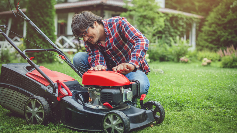 man inspecting red lawn mower