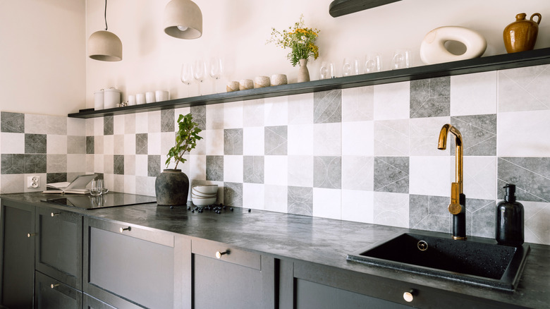 Gray kitchen countertops with black, gray, and white checkered backsplash, exposed shelves, glassware.
