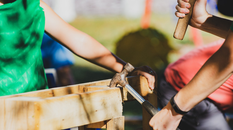 two people disassembling a wooden pallet with the back of a hammer