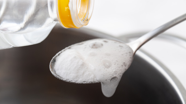 Baking soda bubbles in a spoon after vinegar is poured from a bottle.