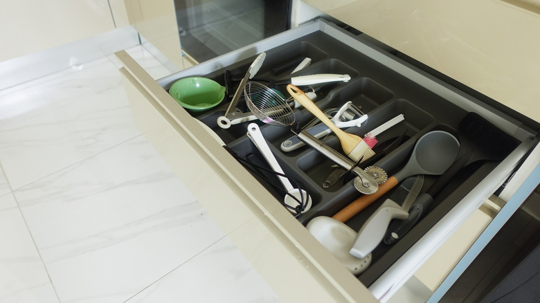 A messy kitchen drawer full of cooking utensils, including a green plastic measuring cup.