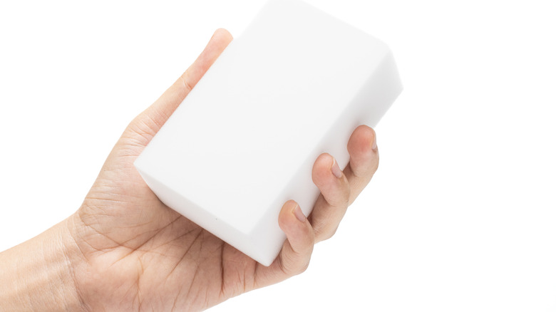 Hand holding a melamine foam sponge on a white background