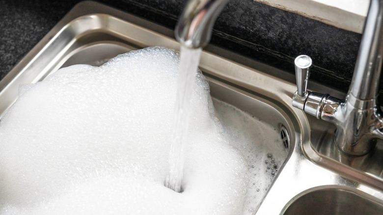 Faucet running into stainless steel sink full of soap bubbles