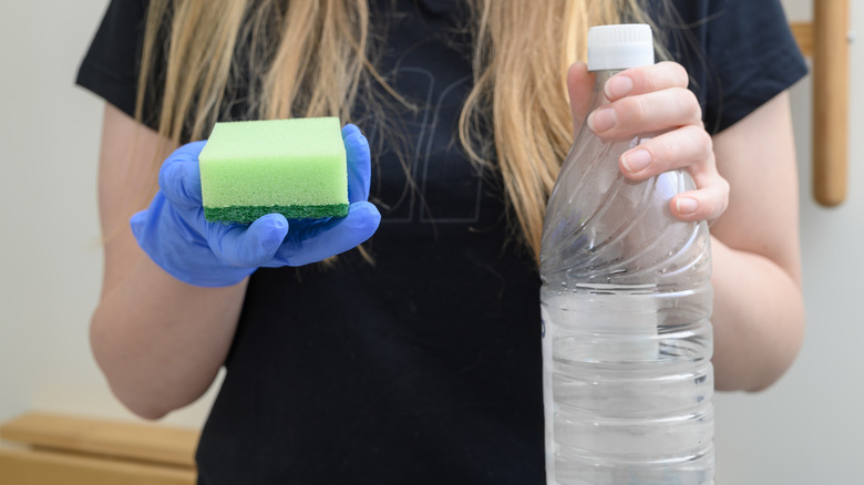 Blonde woman holding bottle of vinegar and a sponge