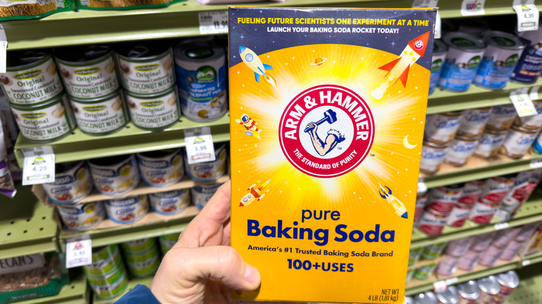 Hand holding box of baking soda in a store aisle
