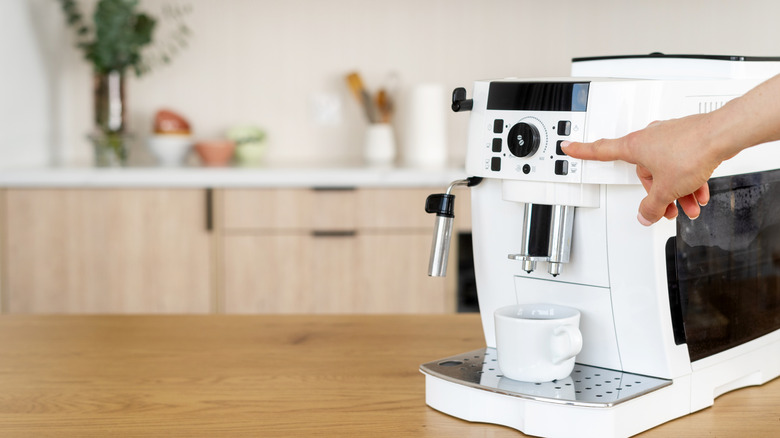 Person pressing the brew button on a white coffee machine