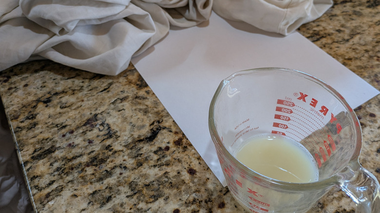 A measuring cup filled with lemon juice and a pile of dirty white sheets sits next to a piece of paper for color comparison.