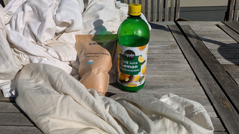 A pile of dirty white sheets sit behind a package of laundry tablets and a bottle of lemon juice.