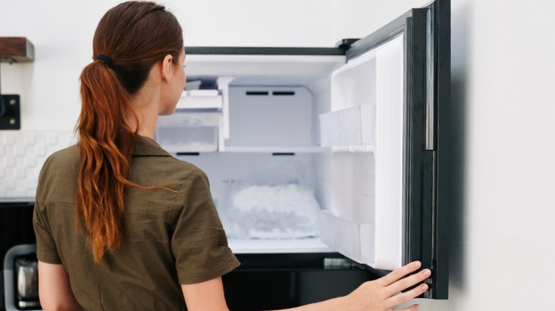 Person opening freezer on black refrigerator.