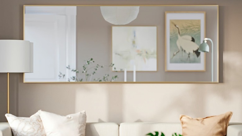The IKEA HOVET mirror with a gold frame hung horizontally on a wall behind a sofa