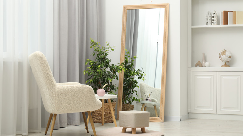 A large mirror leaning against a wall in front of an armchair and plant