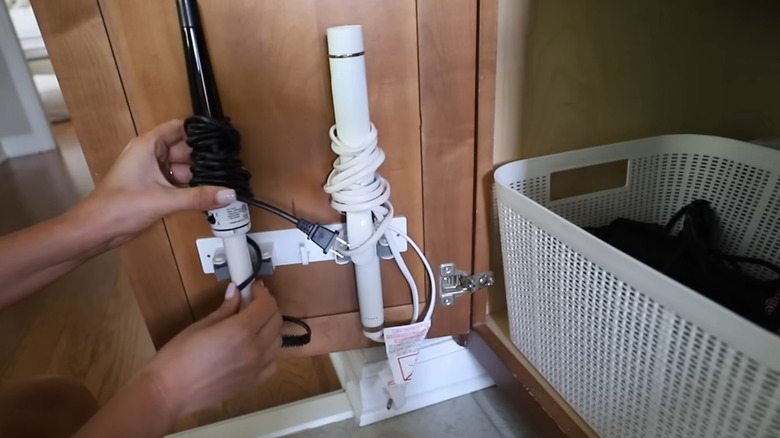 Woman's hand attaching curling irons inside of an adhesive broom holder on interior cabinet door
