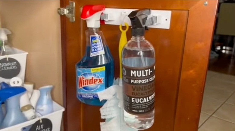 Windex and multi-purpose cleaner hung via broom holder inside of a cabinet