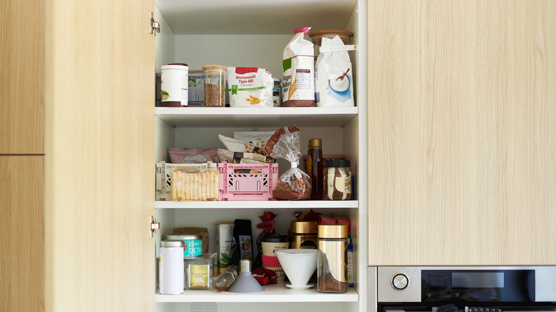 An open kitchen cabinet, packed with food items like flour and coffee