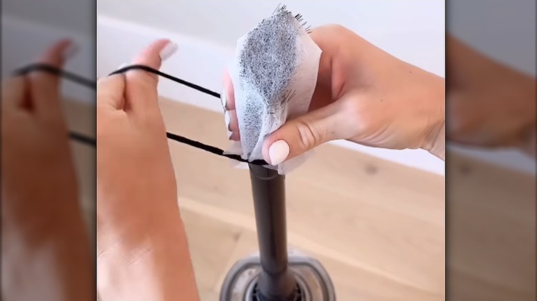 A person tying a dryer sheet of the vacuum cleaner brush
