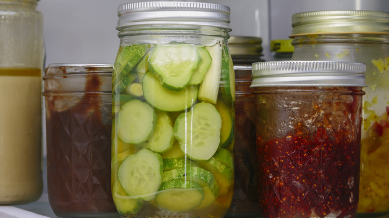Jars of pickles, jams and apple butter inside of a refridgerator.