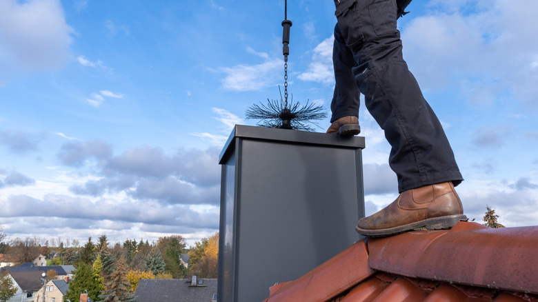 A chimney sweep lowers cleaning equipment into a flue