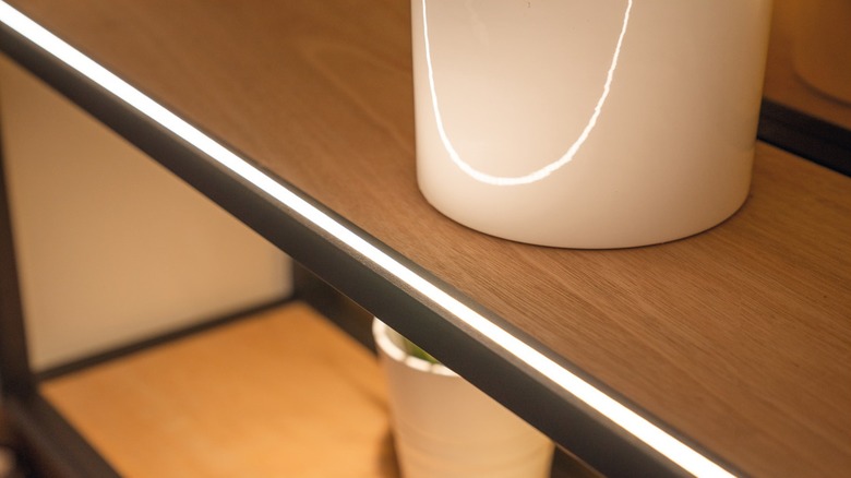An LED strip lights the inside of a cabinet with wooden shelves
