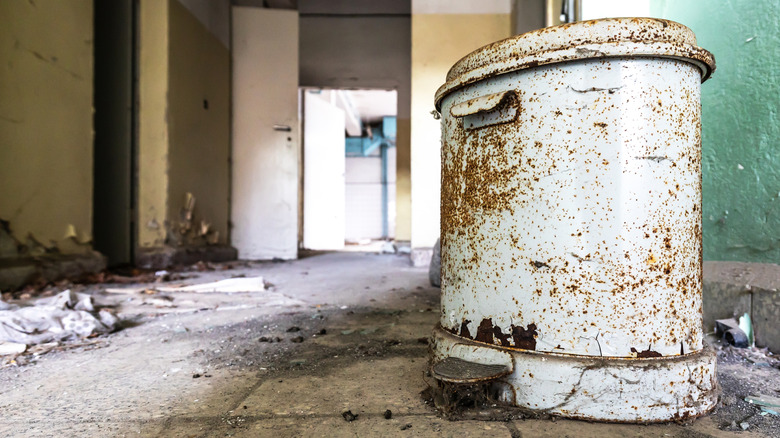 A rusty garbage can sits on the floor of an old house