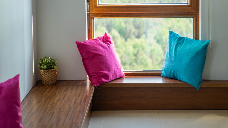 A wood corner bench with pink and blue throw pillows