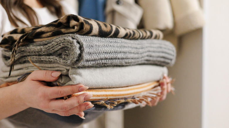 A person holding a stack of folded patterned blankets