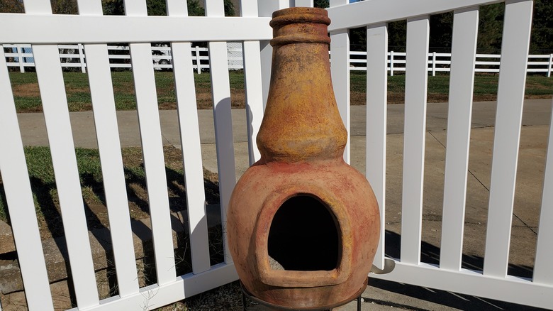 Old chiminea sitting against white picket fence
