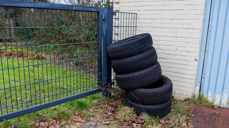 A stack of tires in a backyard leaning against a metal fence