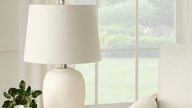 A white ceramic jar table lamp on a table next to a white chair