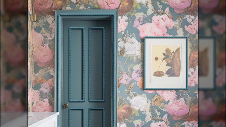 A bedroom wall has flowered wallpaper and a blue-green door covered in beaded wood trim.