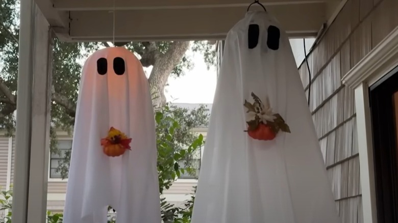 Two decorative ghosts made from Dollar Tree items hang on a porch.