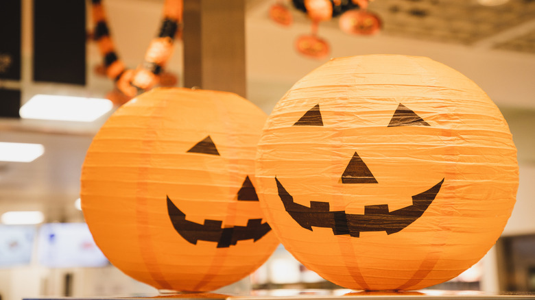 Two orange paper lanterns are painted to look like jack-o'-lanterns.