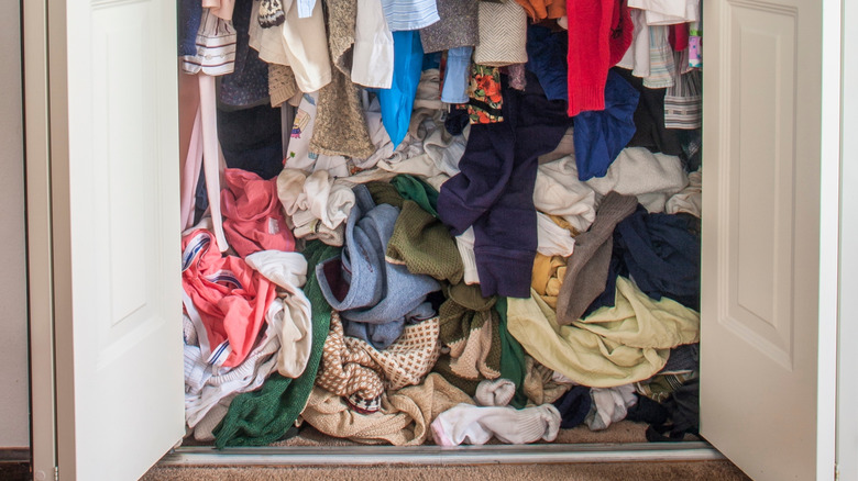 A messy closet, filled with cloths stuffed underneath hanging shirts.