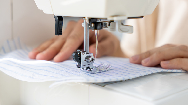 Someone using a white sewing machine to sew white fabric with blue stripes.