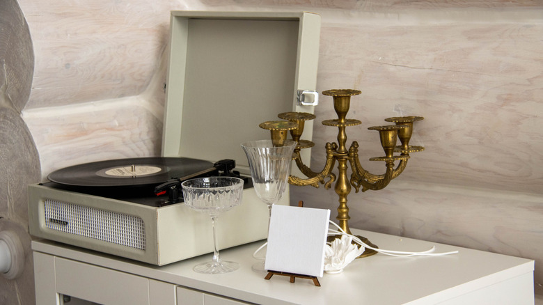 A vintage candelabra on a white cabinet next to a turntable, glasses, and a tiny easel