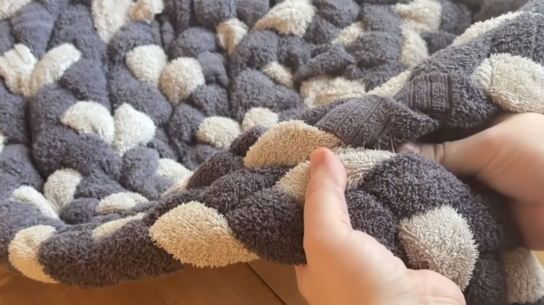 Hands sewing pieces of old towel that have been braided together to make a bathroom floor mat.