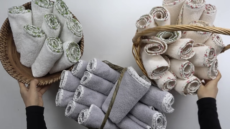 Hands placing several baskets of homemade wash cloths onto a bathroom countertop.