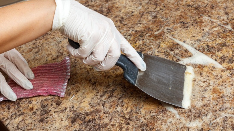 Person cleaning granite countertop with scraper tool