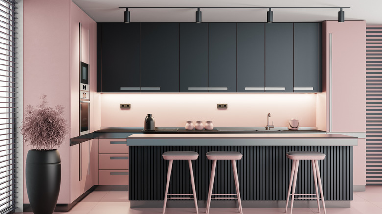 A kitchen with black and pink cabinets, pink walls, and pink stools at a black counter