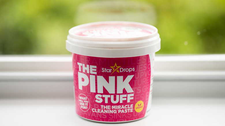 A jar of The Pink Stuff on a counter in front of a window with blurry green foliage behind it