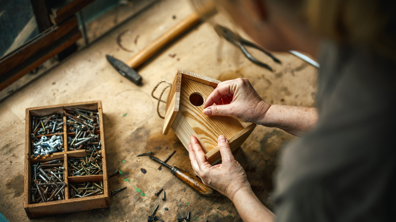 woman building a wooden birdhouse in shop with tools around