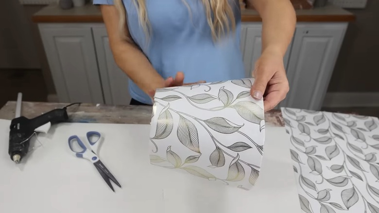 Woman wrapping gold and white wallpaper around plant pot.