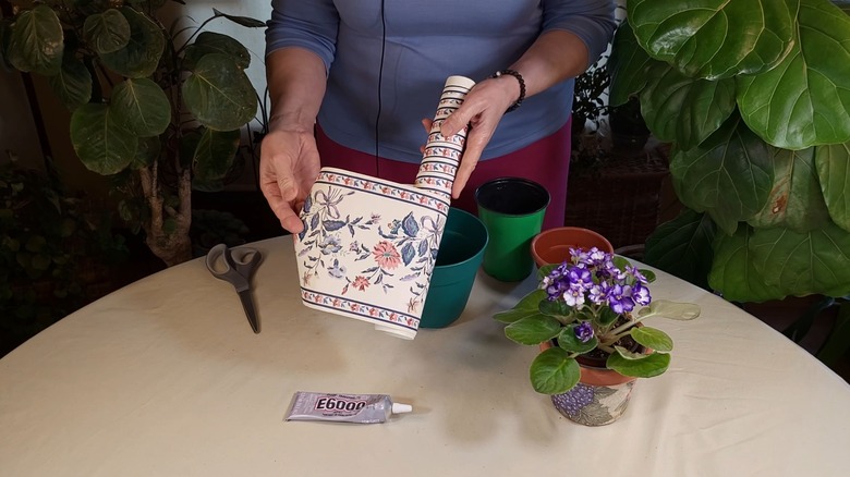Woman with roll of floral wallpaper and plain plant pots.