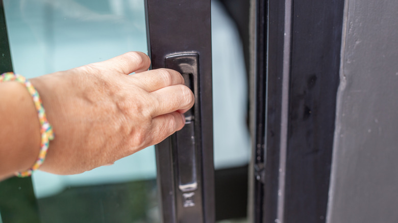 A hand pulling open a sliding glass door from the handle
