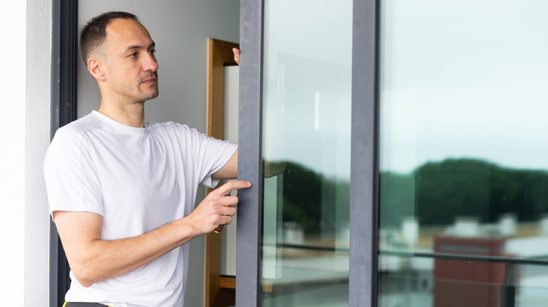 A man with a white shirt and yellow and black tool belt working on a sliding glass door