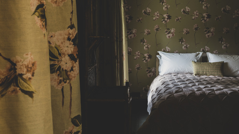 A bedroom with dark floral wallpaper and curtains