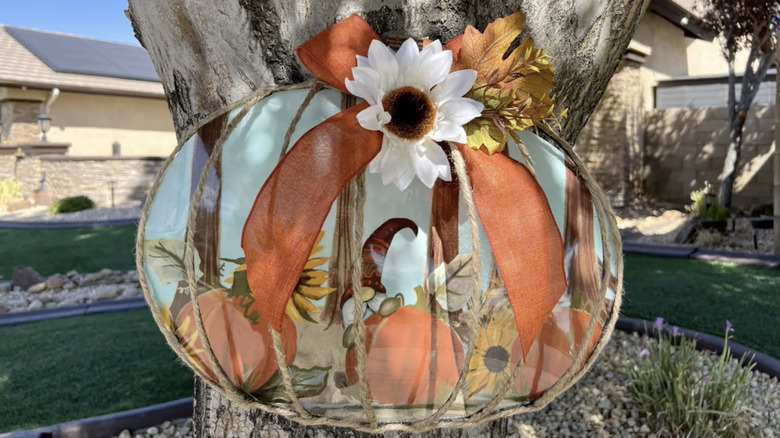A DIY fall pumpkin wreath decorated with twine, ribbon, and artificial fall flowers