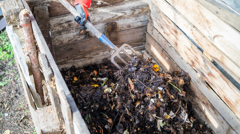 Hand using a small pitchfork to turn compost in a wooden bin