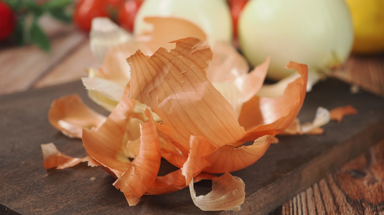 Onion peels on a cutting board with white onions and tomatoes behind them