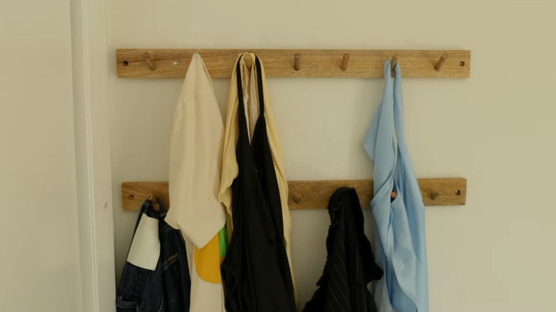 Two wooden coat racks with pegs hanging on the wall with laundry on several of the pegs