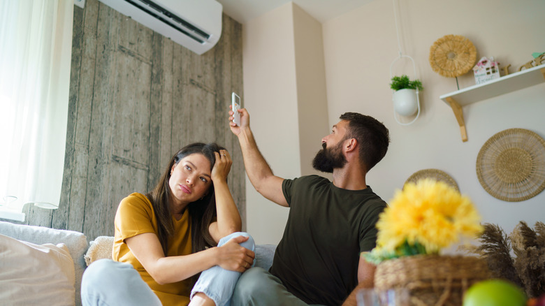 A couple bothered by the weather and the man turning the AC on.